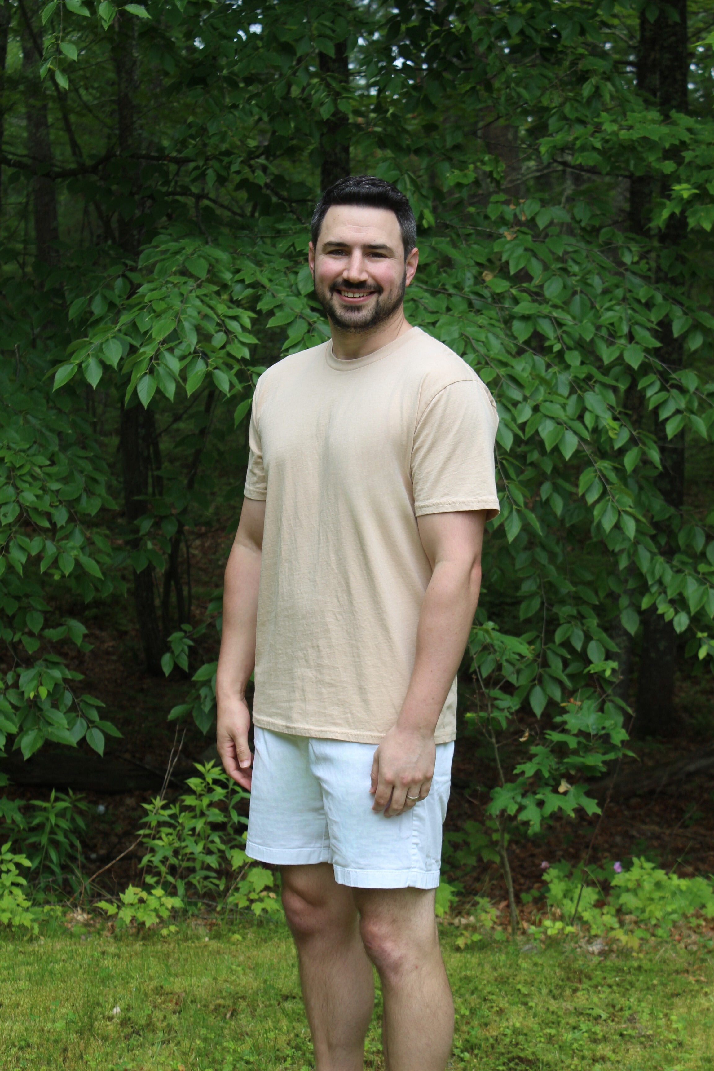 Man wearing a light beige organic cotton t-shirt and white shorts in a natural outdoor setting.