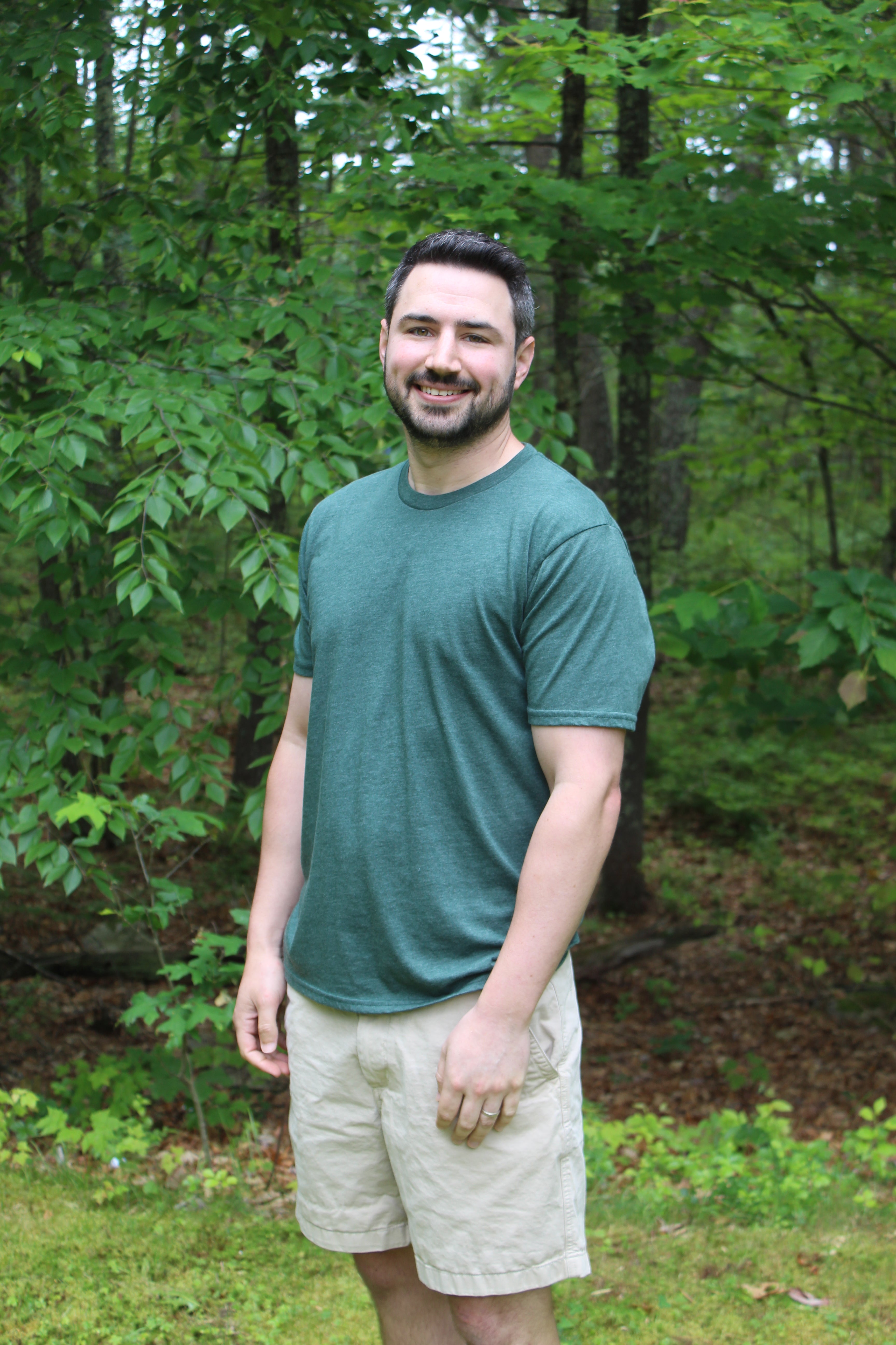 Man wearing a green organic cotton tee and shorts standing in a lush outdoor setting.