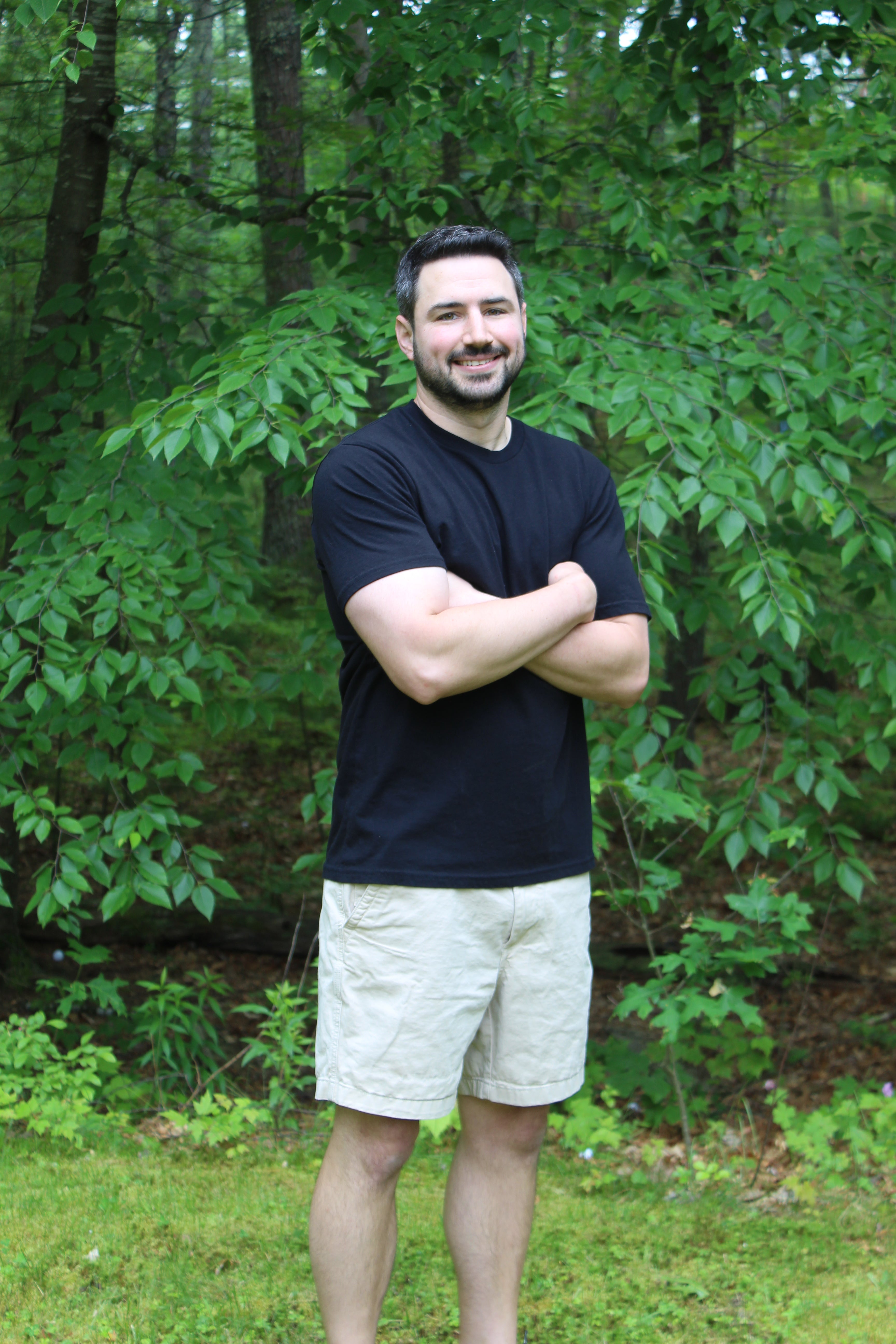 Man smiling outdoors in a black organic cotton tee, showcasing durability and comfort in a natural setting.
