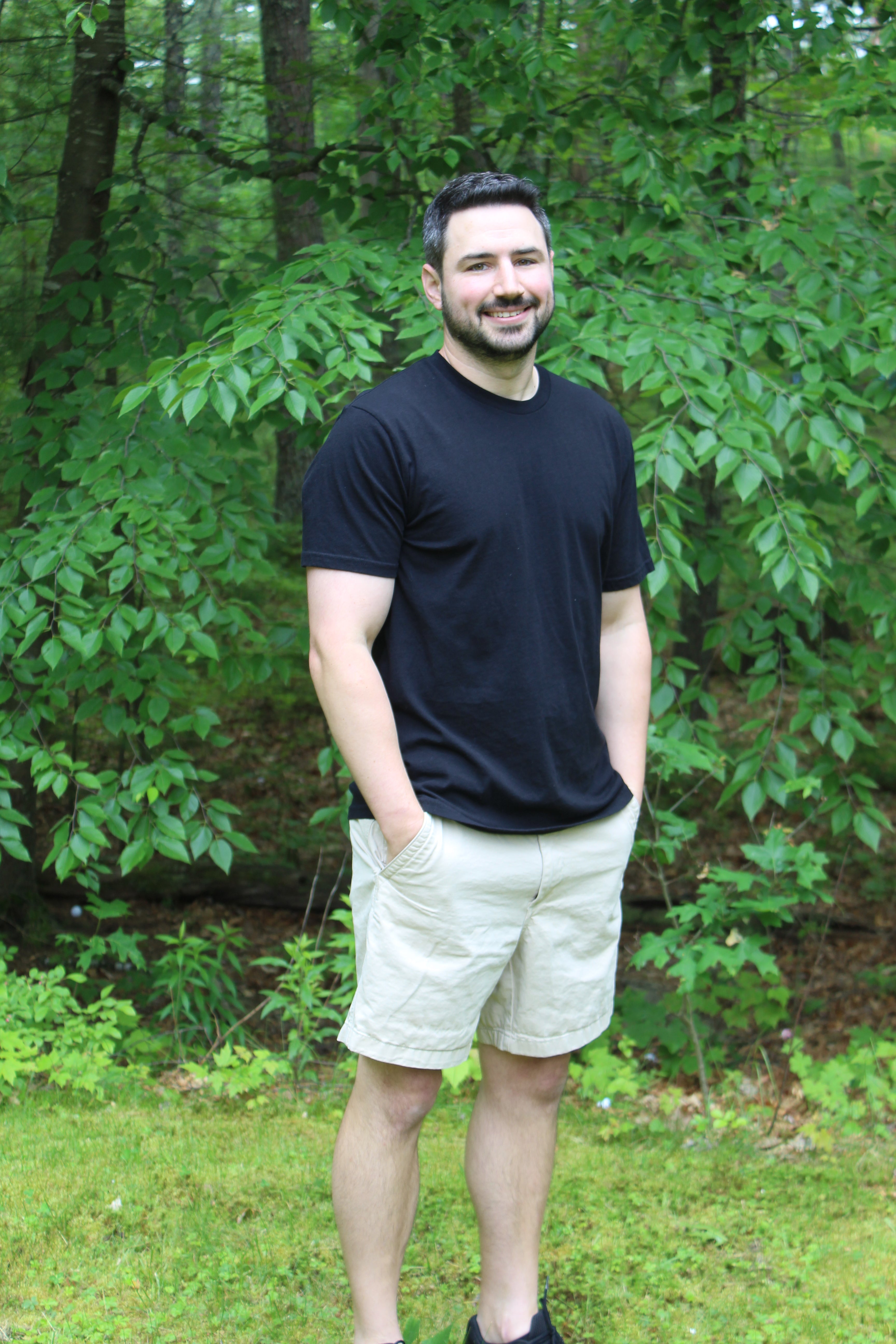 Man wearing a black organic cotton tee and shorts in a lush green outdoor setting.