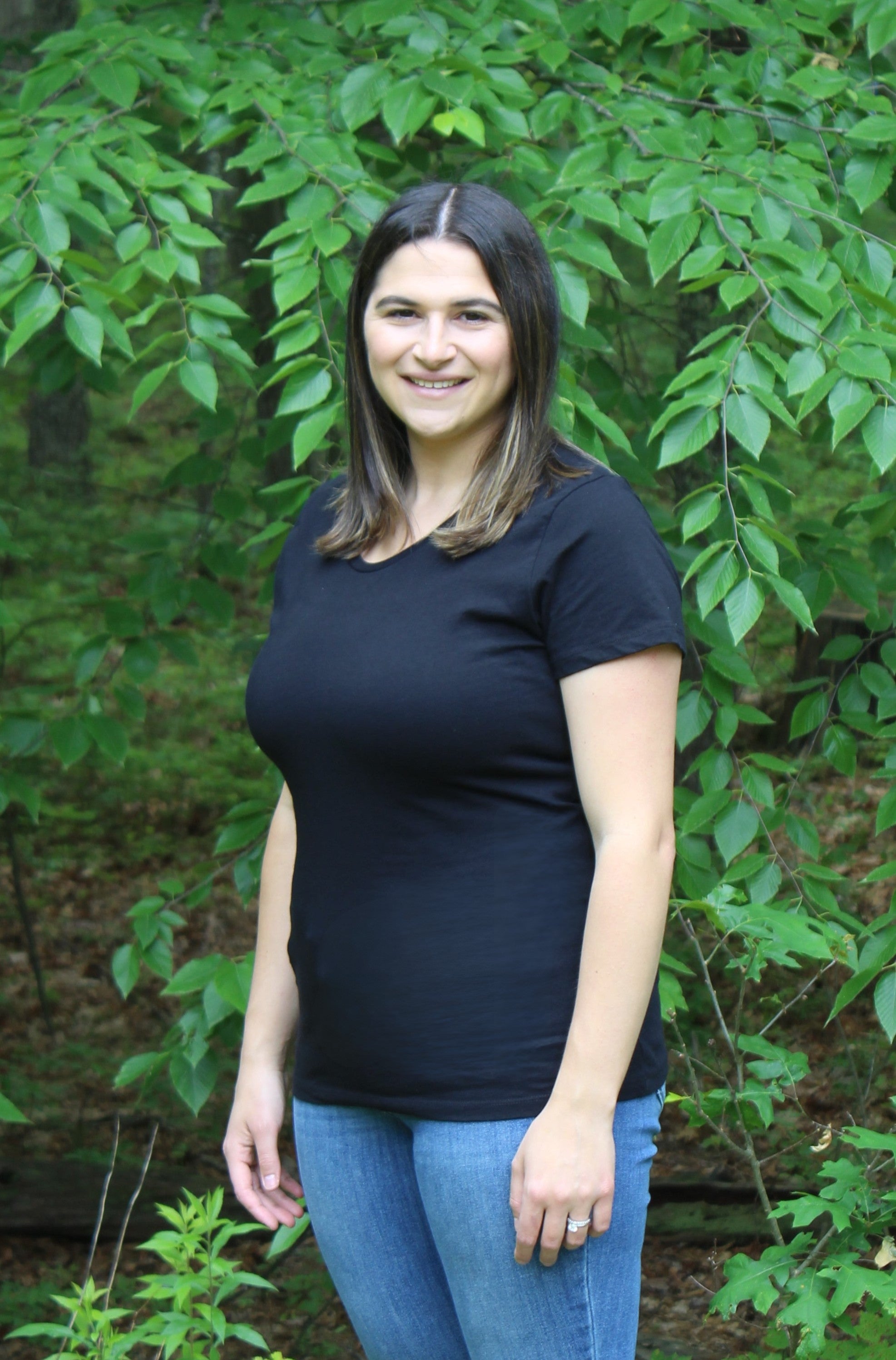 Woman wearing a black fitted tee made from 100% organic cotton, surrounded by green foliage, showcasing comfort and style.